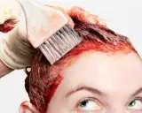 Application d'une teinture rouge pour un nouvel effet couleur cheveux. Une main gantée utilise un pinceau pour colorer les racines.