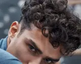 Gros plan sur un homme avec une coupe homme mi long bouclé, ses boucles sombres encadrant son visage.