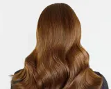 Chevelure brune aux reflets chauds, un balayage chatain clair subtil illumine ces ondulations douces.