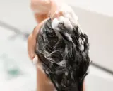 Mousse de shampoing sans silicone, une main masse le cuir chevelu sous une douche.
