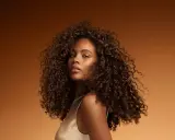 Une jeune femme aux cheveux bouclés et brillants, un exemple de comment bien rincer ses cheveux pour un éclat naturel.
