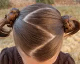 Cheveux bruns tressés en deux couettes rondes, séparés par une raie zig zag.