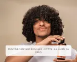Un homme aux cheveux bouclés tient un flacon de shampoing, parfait pour l'hydratation cheveux bouclés.