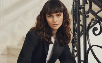 Une femme au regard intense arbore un **wolf cut cheveux bouclés** brun, porté avec un blazer noir.