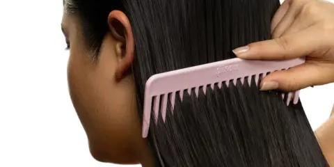 Une main peigne de longs cheveux noirs avec un peigne rose. Pas de nœud dans les cheveux, juste une chevelure soyeuse.