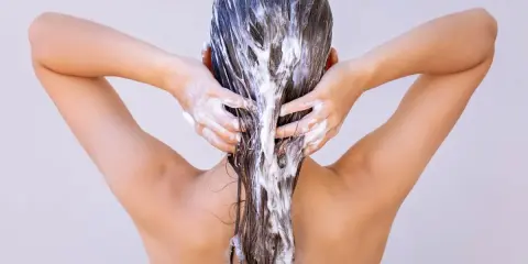 Dos mains appliquent un masque capillaire sur des cheveux longs et bruns. Attention à ne pas laisser poser un masque cheveux trop longtemps !