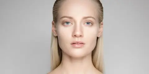Portrait d'une jeune femme aux yeux bleus et aux cheveux gominés, mise en valeur par une lumière douce.