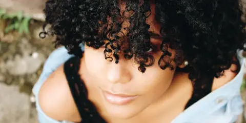 Une jeune femme aux cheveux bouclés naturels, une coiffure cheveux bouclés facile et magnifique, porte une veste en jean.