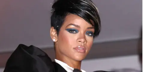 Une femme arbore une coupe femme carré rasé coté, avec un maquillage audacieux et une tenue élégante.