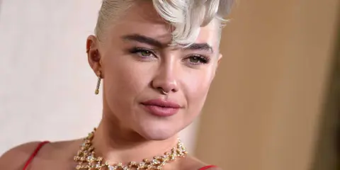 Une femme arbore une coupe courte blonde tendance, ornée d'un collier scintillant et d'une robe rouge.