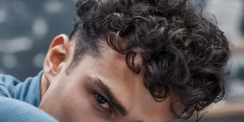 Gros plan sur un homme avec une coupe homme mi long bouclé, ses boucles sombres encadrant son visage.