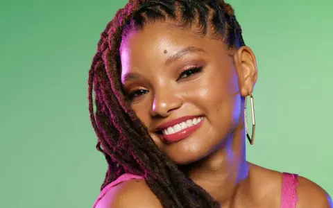 Jeune femme souriante avec une coiffure avec bijoux cheveux, des dreadlocks ornées de reflets violets, et de grandes boucles d'oreilles dorées.