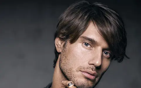 Un homme au regard intense, coiffé décoiffé, porte une bague ornée d'un motif discret.