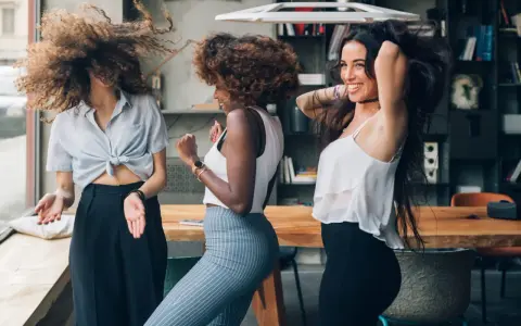 Trois femmes aux cheveux bouclés dansent joyeusement. Leurs chevelures volent, un exemple de comment avoir de belles boucles sans frisottis.