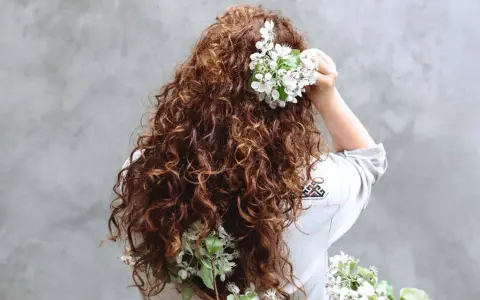 Chevelure brune et bouclée ornée de fleurs blanches, évoquant un décollement de racine naturel et printanier.