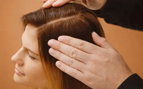 Mains caressant des cheveux châtains, séparés en deux sections. Une femme regarde vers le bas, l'air pensif, peut-être à cause de ses cheveux moches.