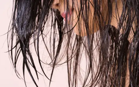 Cheveux sombres et humides tombant en cascade, révélant un aperçu d'une bouche rose et d'une peau claire.