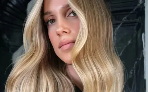 Une femme aux yeux verts et aux lèvres pulpeuses arbore une chevelure ondulée d'une magnifique teinte de blond.