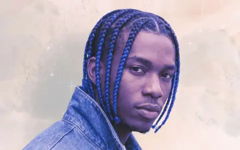 Un jeune homme aux tresses bleues éclatantes, portant une veste en jean, pose avec confiance.