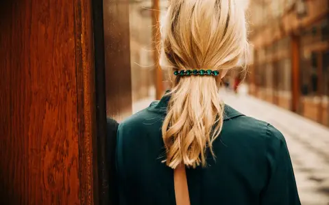 Coiffure avec barrette ornée de pierres vertes, retenant une queue de cheval blonde.