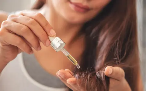 Une main applique une goutte d'huile sur la pointe des cheveux pour les nourrir.