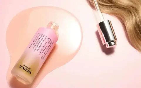 Sérum pour cheveux Madame d'Alexis, promettant des cheveux mousseux et nourris. Une goutte de produit tombe près d'une mèche blonde.