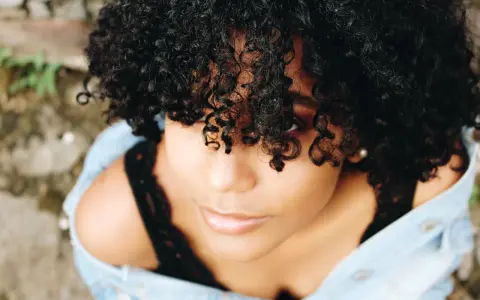 Une jeune femme aux cheveux bouclés naturels, une coiffure cheveux bouclés facile et magnifique, porte une veste en jean.