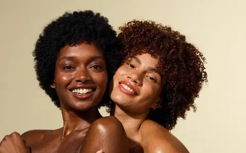 Deux femmes souriantes, l'une avec des cheveux crépus 4c noirs, l'autre avec des boucles rousses.