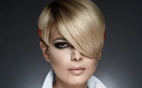 Une femme au regard intense arbore une coupe au bol audacieuse, avec des mèches blondes et des pointes orangées.
