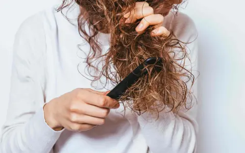 Une personne démêle ses cheveux mouillés et **cheveux emmêlés à la racine** avec un peigne noir.