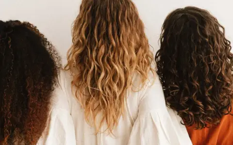 Trois femmes montrent leurs cheveux bouclés abîmés, de différentes couleurs et textures, sur fond blanc.