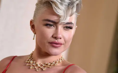 Une femme arbore une coupe courte blonde tendance, ornée d'un collier scintillant et d'une robe rouge.