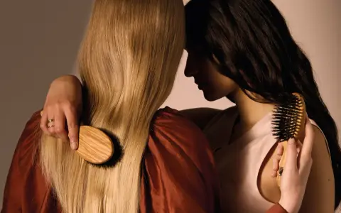 Deux femmes se serrent, l'une brosse les cheveux blonds de l'autre avec une brosse en bois.