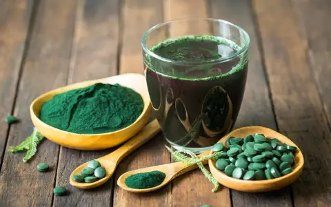 Spiruline en poudre, comprimés et boisson verte sur fond de bois. Découvrez les bienfaits spiruline cheveux pour une chevelure éclatante.