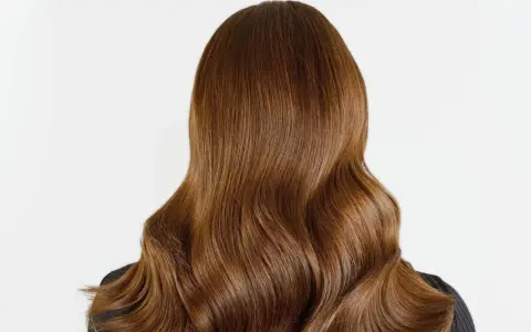 Chevelure brune aux reflets chauds, un balayage chatain clair subtil illumine ces ondulations douces.
