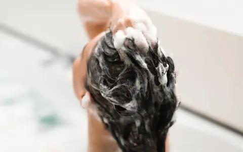 Mousse de shampoing sans silicone, une main masse le cuir chevelu sous une douche.