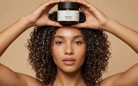 Une femme aux cheveux bouclés tient un pot de masque perfecteur de boucles au beurre de karité au-dessus de sa tête.