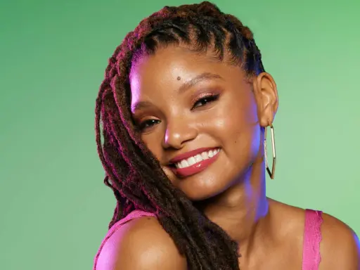 Jeune femme souriante avec une coiffure avec bijoux cheveux, des dreadlocks ornées de reflets violets, et de grandes boucles d'oreilles dorées.