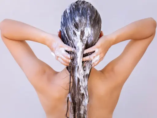 Dos mains appliquent un masque capillaire sur des cheveux longs et bruns. Attention à ne pas laisser poser un masque cheveux trop longtemps !
