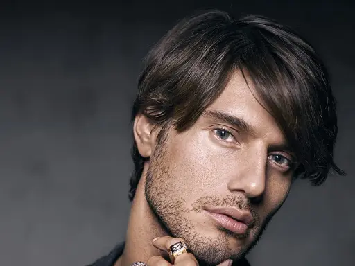 Un homme au regard intense, coiffé décoiffé, porte une bague ornée d'un motif discret.