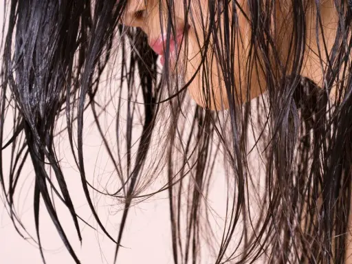 Cheveux sombres et humides tombant en cascade, révélant un aperçu d'une bouche rose et d'une peau claire.