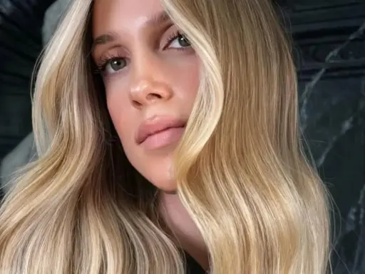 Une femme aux yeux verts et aux lèvres pulpeuses arbore une chevelure ondulée d'une magnifique teinte de blond.
