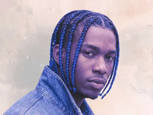 Un jeune homme aux tresses bleues éclatantes, portant une veste en jean, pose avec confiance.