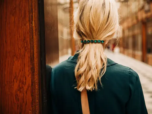 Coiffure avec barrette ornée de pierres vertes, retenant une queue de cheval blonde.