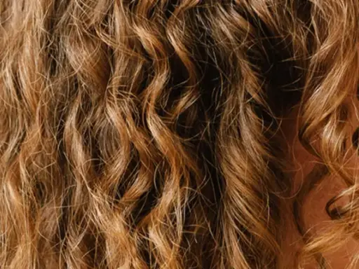 Une femme se coiffe les cheveux ondulés le matin, révélant des boucles dorées et un sourire radieux.