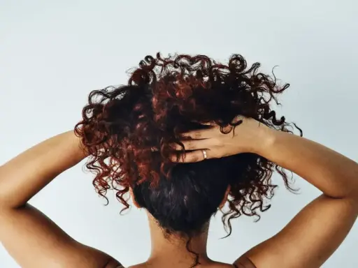 Cheveux bouclés, comme après une baignade dans l'eau salée, sont coiffés par des mains sur fond blanc.