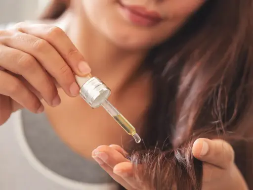 Une main applique une goutte d'huile sur la pointe des cheveux pour les nourrir.