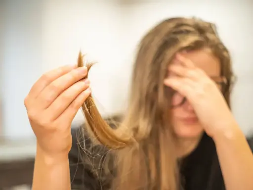 Une main tient une mèche de cheveux, visiblement abîmés, comme si c'était du cheveux mort. La personne semble désespérée.
