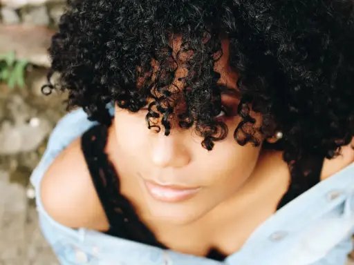 Une jeune femme aux cheveux bouclés naturels, une coiffure cheveux bouclés facile et magnifique, porte une veste en jean.