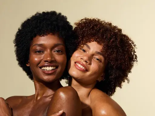 Deux femmes souriantes, l'une avec des cheveux crépus 4c noirs, l'autre avec des boucles rousses.